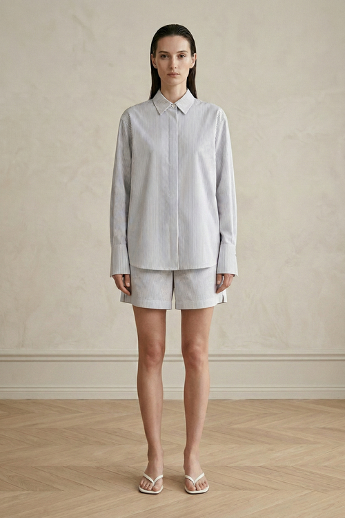 Woman wearing a light blue shirt and beige shorts against a neutral background