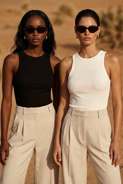 Two women standing side by side in a desert setting, wearing sunglasses and casual outfits.