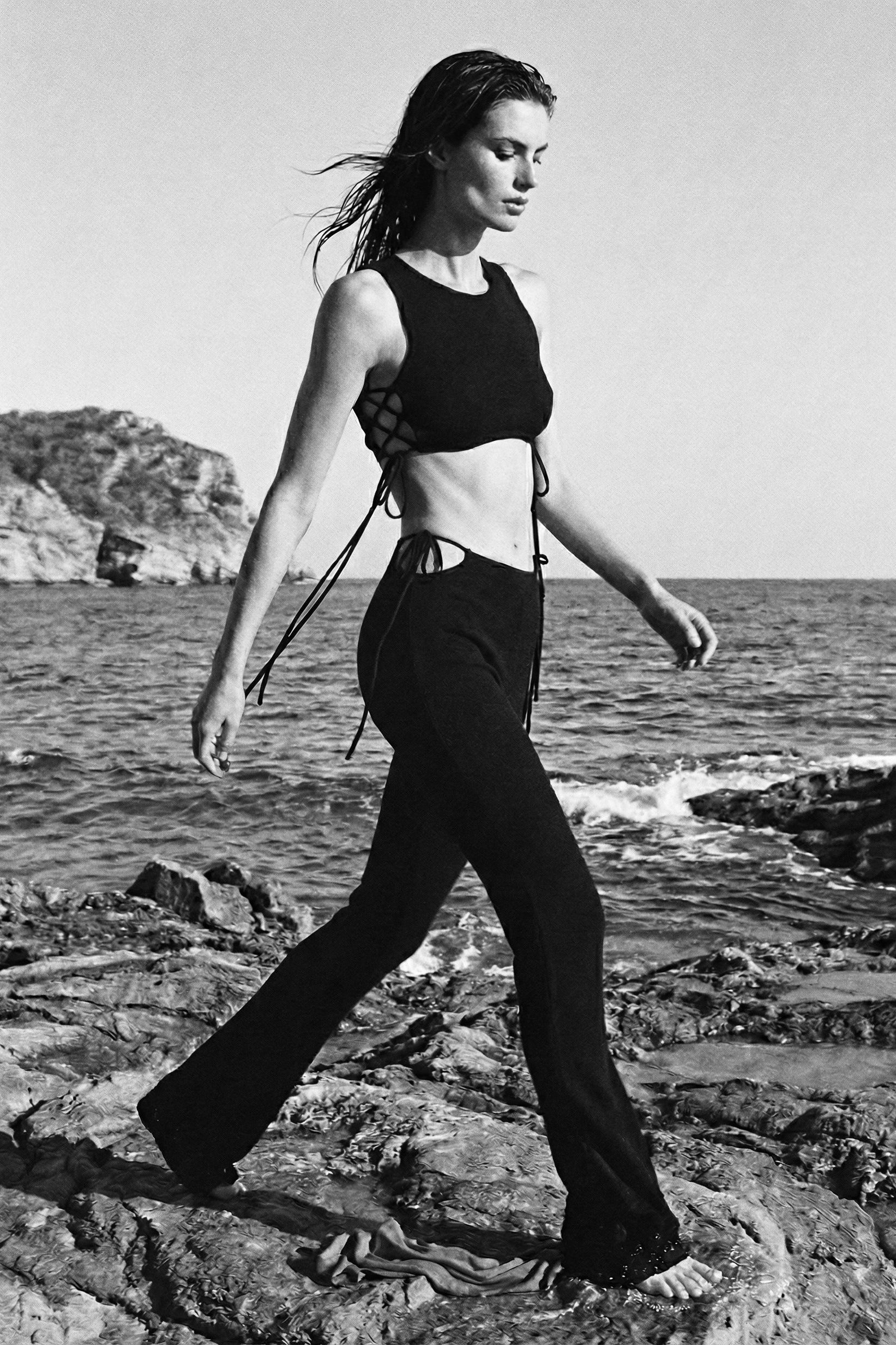 Woman walking on rocks by the sea wearing a black outfit.