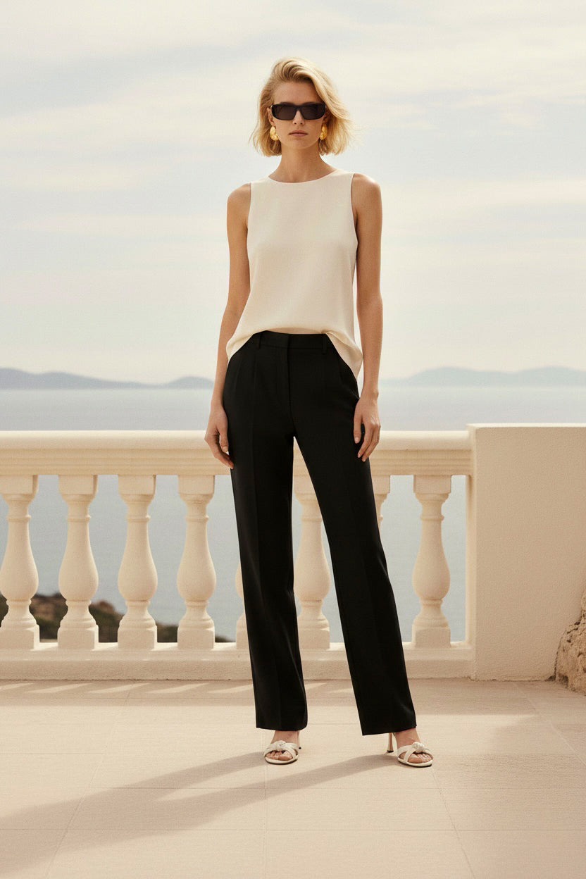 Woman in a white sleeveless top and black pants standing on a balcony with a scenic view.
