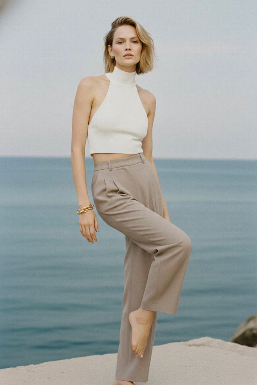 Woman in a white top and beige pants standing by the ocean