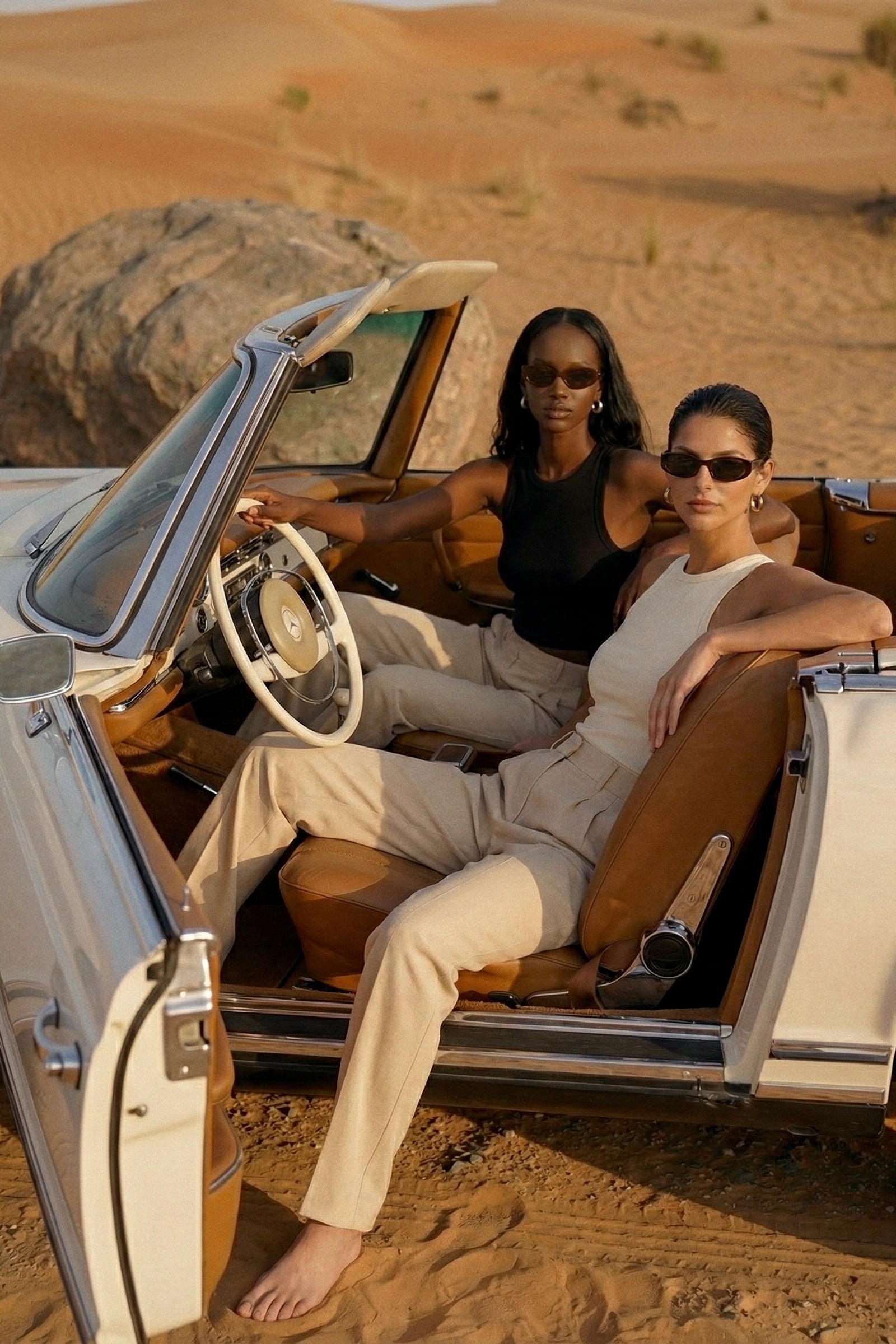 Two women sitting in an open-top car in a desert setting