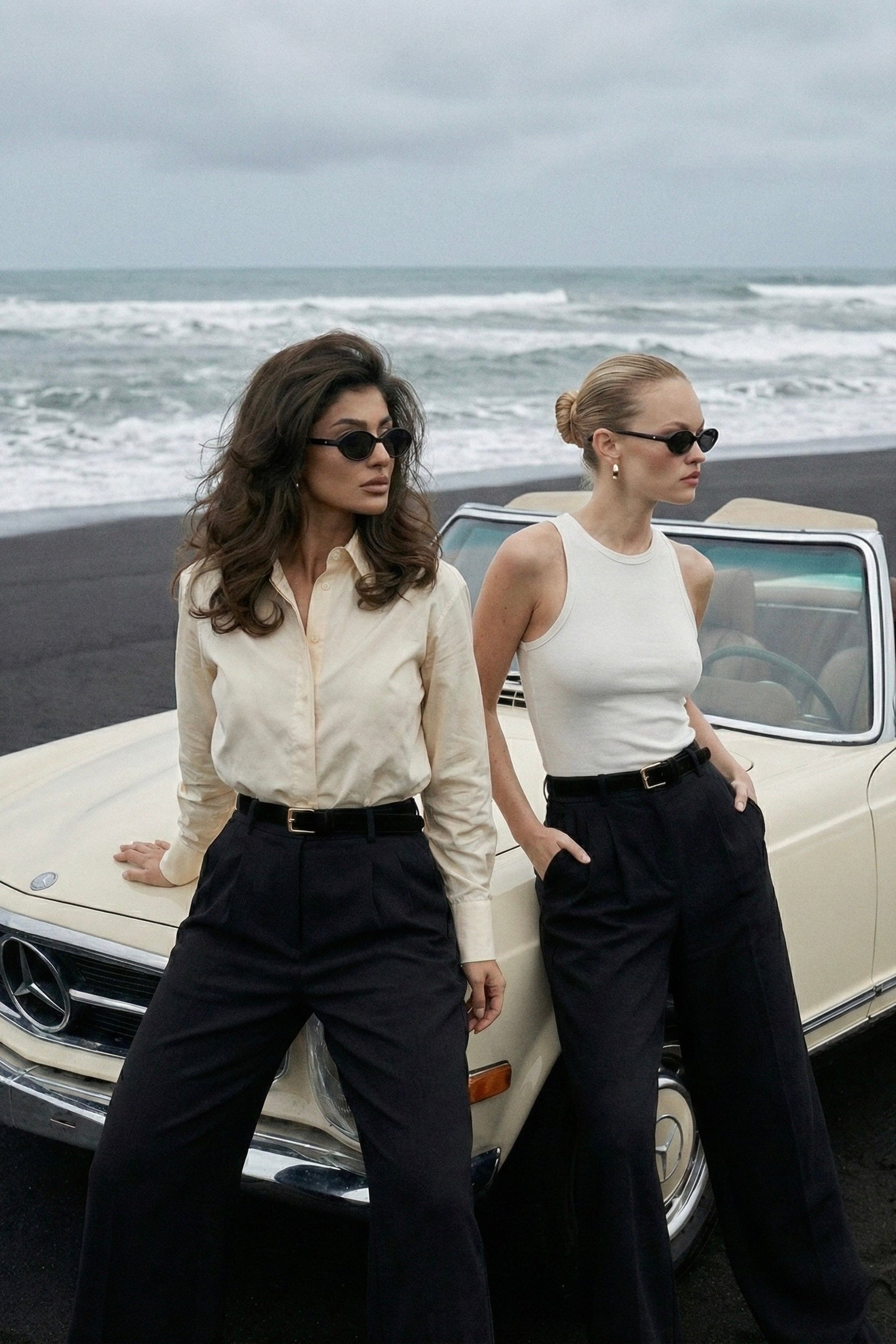 Two women standing by a vintage Mercedes-Benz car on a beach.