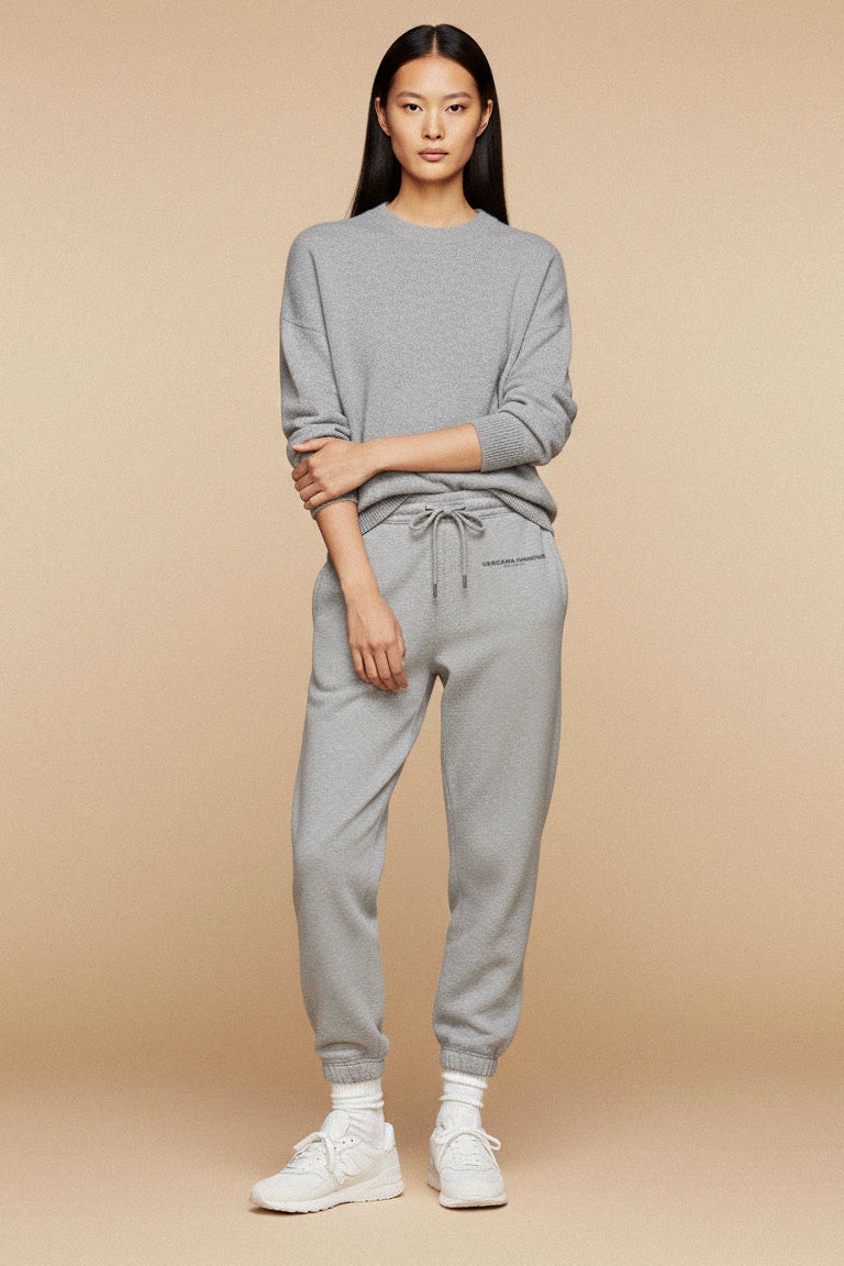 Woman wearing a gray sweatshirt and jogger pants on a beige background